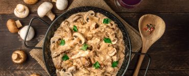 Mushroom beef stroganoff, with cremini and champignons, in a frying pan, shot from above on a dark rustic texture with a place for text and a glass of red wine